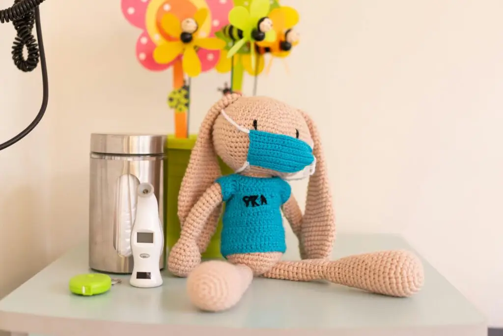 Cozy pediatric clinic decor featuring a knitted toy, digital thermometer, and cheerful flowers.
